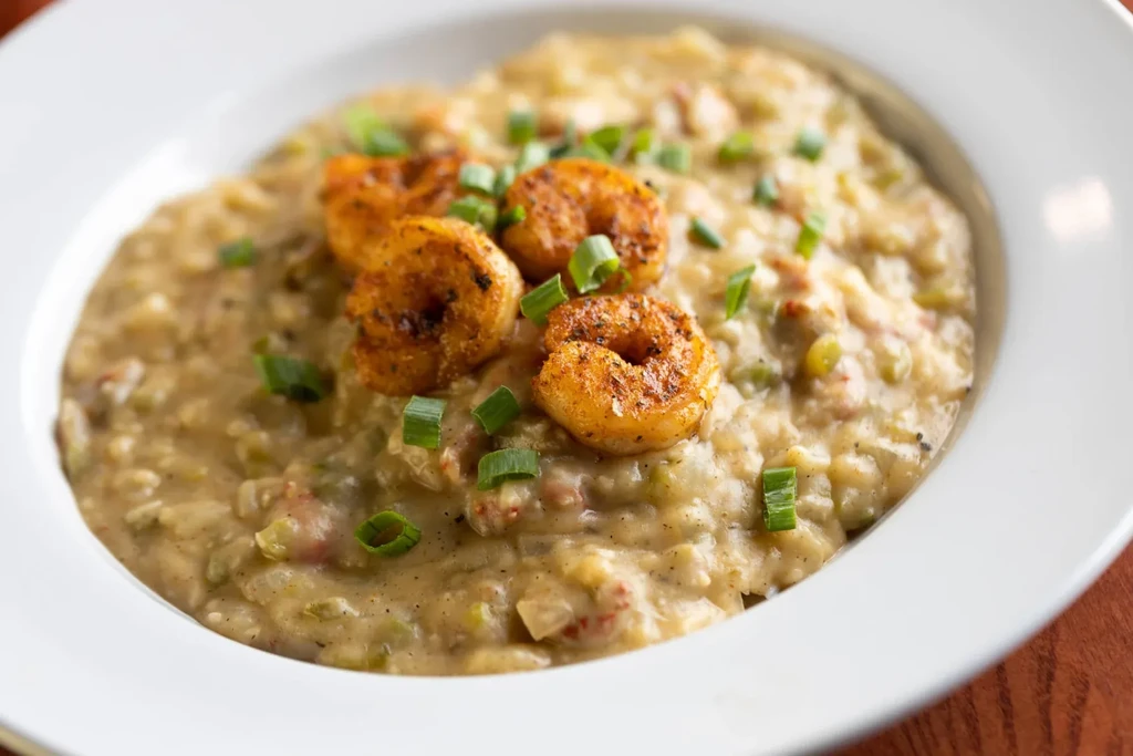 Five pan-seared shrimp on creamy grits with green onion garnish.