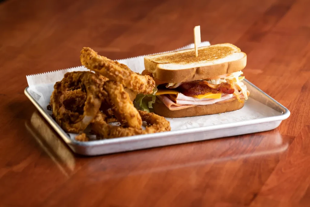 Toasted club sandwich and golden onion rings on a metal tray.