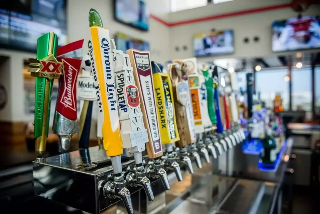 Colorful, branded beer tap handles line a brightly lit bar.