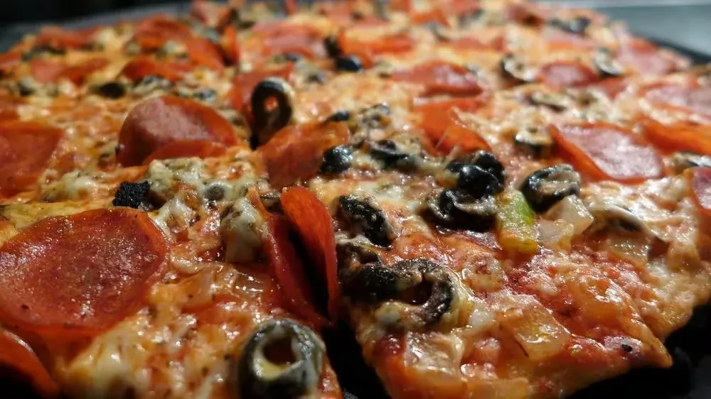Hot, sliced pizza with pepperoni, olives, cheese, and peppers.