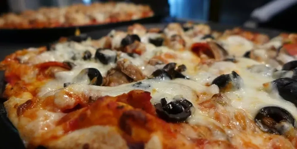 Close-up of golden-crusted pizza with melted cheese, black olives, and sausage.