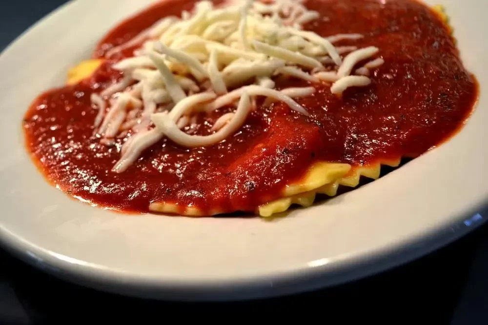 Ravioli with rich tomato sauce and shredded white cheese.
