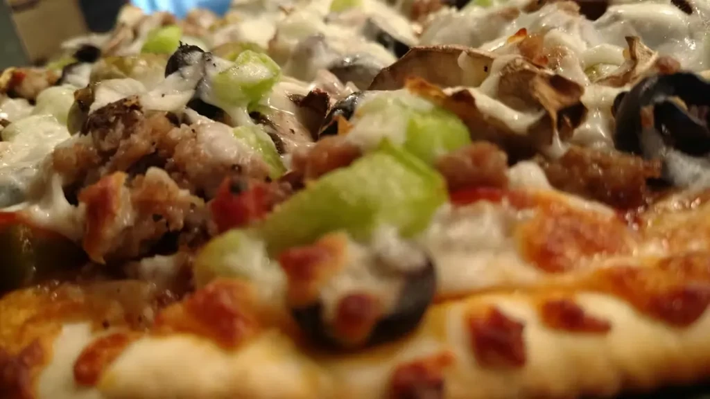 Low-angle close-up of pizza with cheese, sausage, peppers, olives, mushrooms.