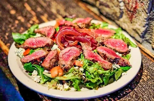 Steak salad with medium-rare slices, green lettuce, cheese, and vegetables.