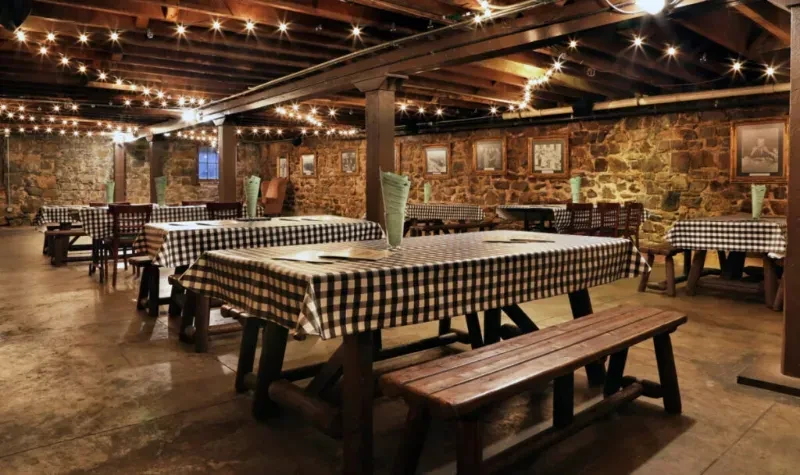 Stone-walled rustic restaurant with checkered tables and warm string lights.