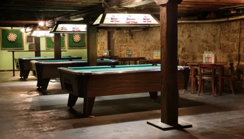 Rustic pub with three Shiner-lit teal pool tables and dartboards.