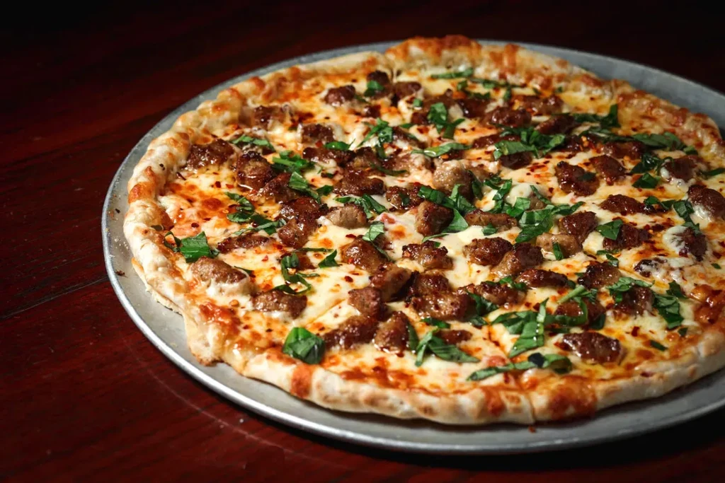 Cooked round pizza with mozzarella, browned sausage, basil, and chili flakes.
