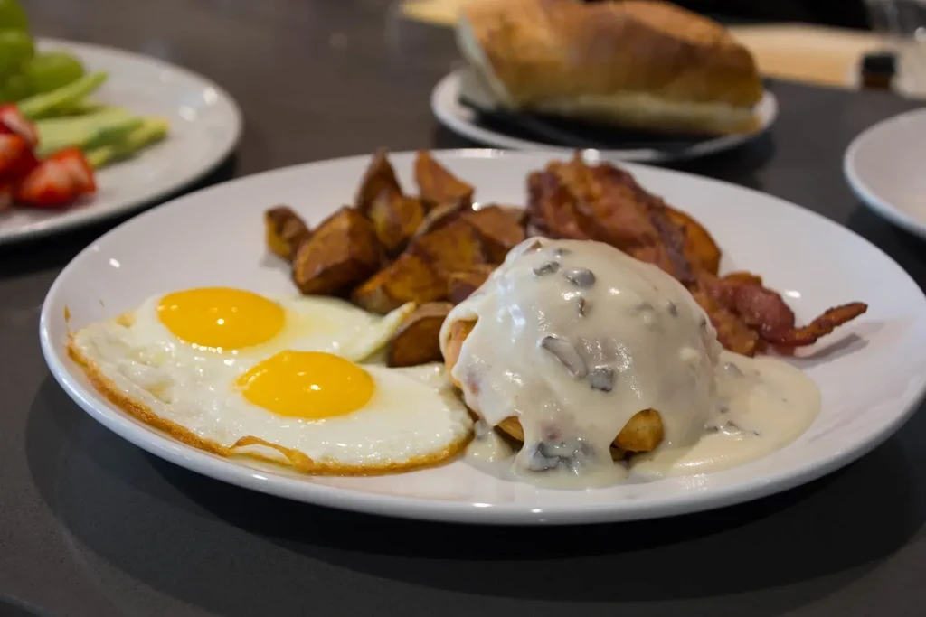 Close-up: fried eggs, bacon, home fries, and a gravy-covered biscuit.