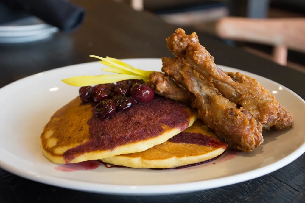 Golden pancakes with berry sauce, crispy fried chicken on a white plate.