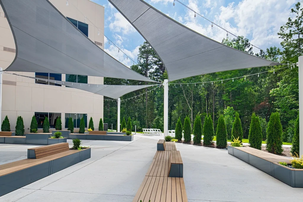 Expansive patio with sail shades, modern benches, and evergreen shrubs.
