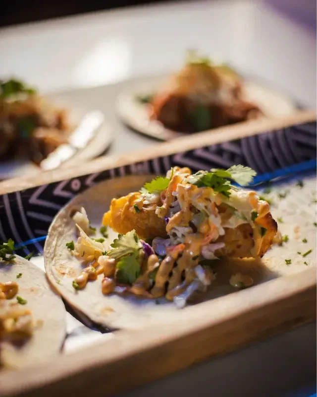Crispy fried tacos with slaw, sauce, and cilantro on a wooden tray.