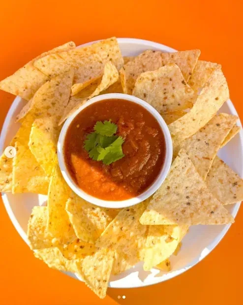 Overhead plate of seasoned tortilla chips with salsa and cilantro on orange.
