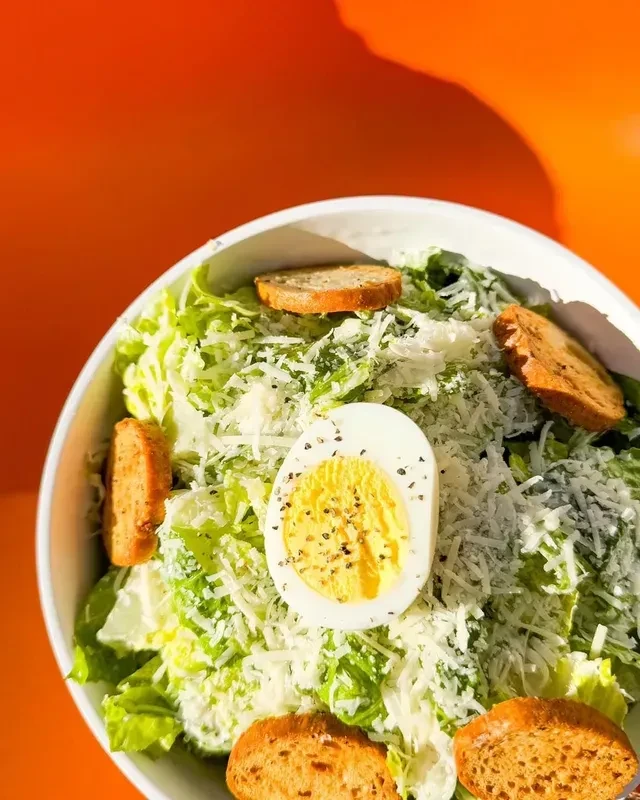 Close-up Caesar salad with hard-boiled egg, croutons, Parmesan, orange background.