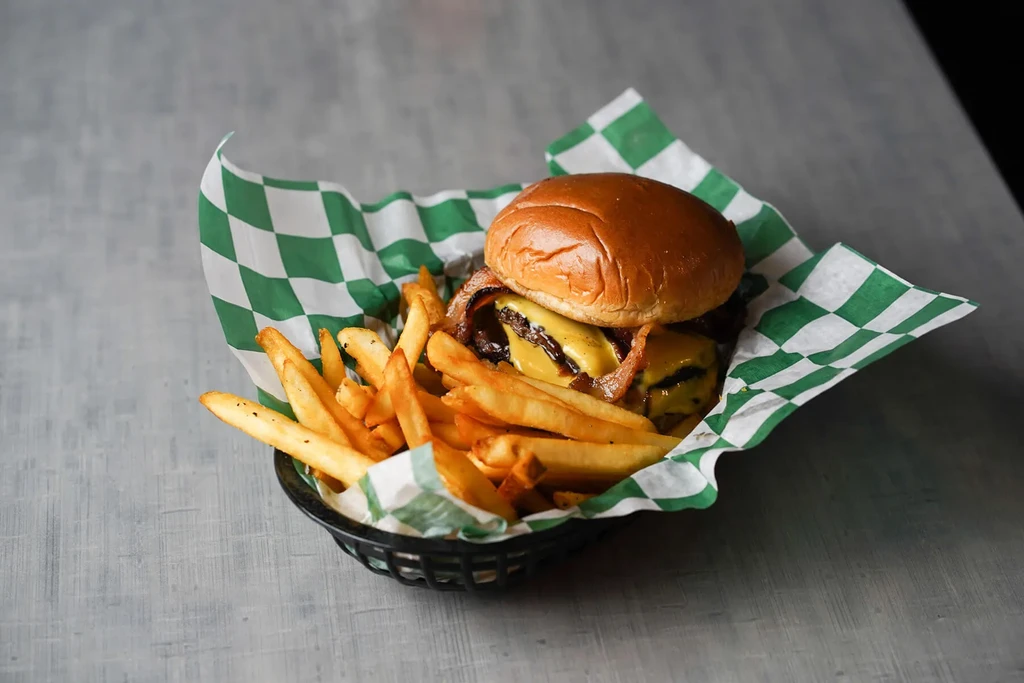 A double bacon cheeseburger and peppered fries in a plastic basket.