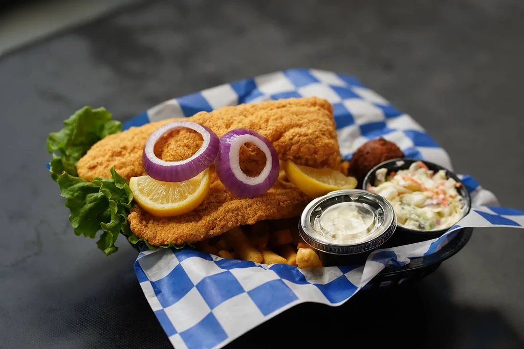 Fried fish, french fries, coleslaw, tartar sauce, and a hush puppy.