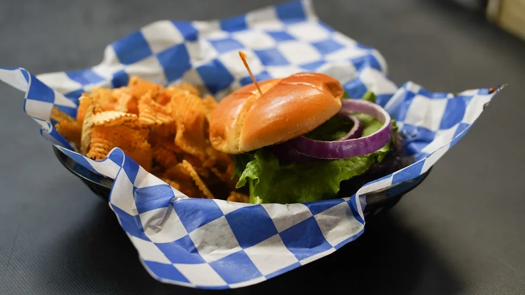 Burger with lettuce, red onion, and seasoned ridged chips in a basket.