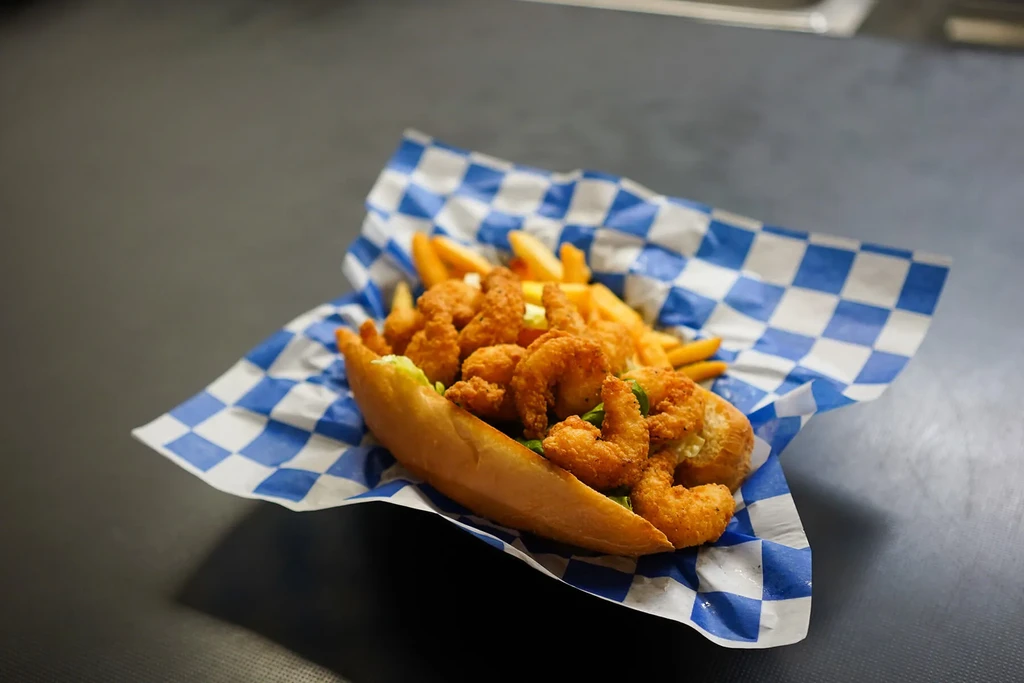 Shrimp po'boy with french fries in a checkered paper-lined holder.