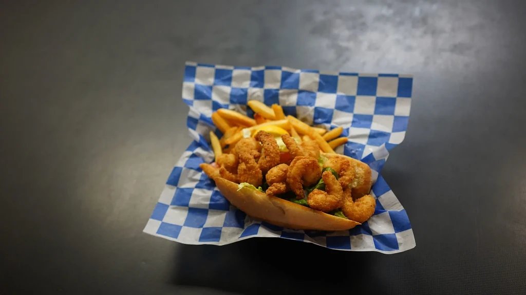 Fried shrimp po'boy, French fries, and lemon on checkered paper.