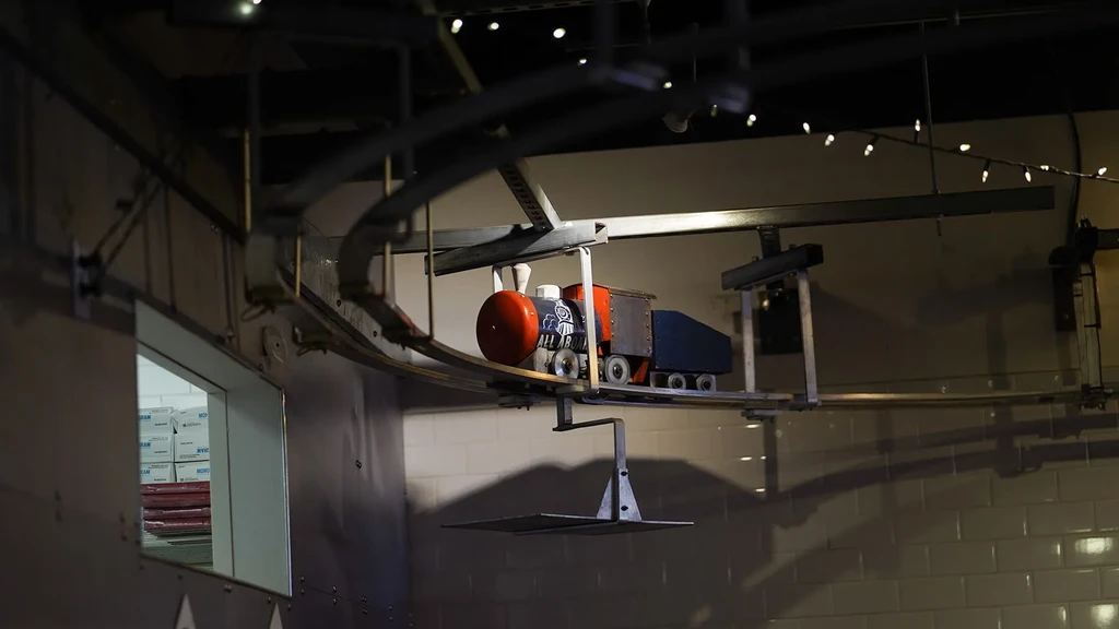 Colorful model train on overhead track delivers items via platform.