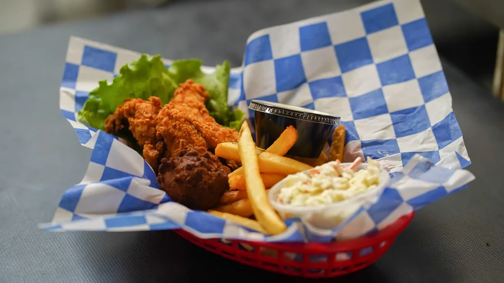 Fried chicken tenders, fries, coleslaw, and sauce in a red basket.
