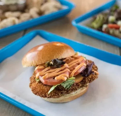 Crispy fried chicken sandwich with lettuce, tomato, sauce on a blue tray.