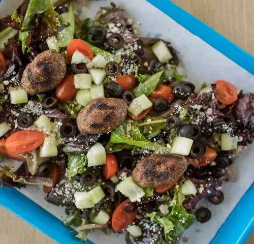 Vibrant salad in blue container with grilled items, tomatoes, and cheese.
