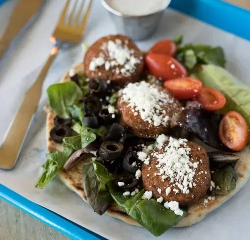 Close-up of falafel with feta, vegetables, and sauce on a blue tray.