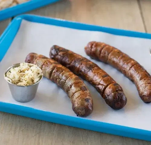 Three grilled sausages and sauerkraut in a blue-rimmed tray.