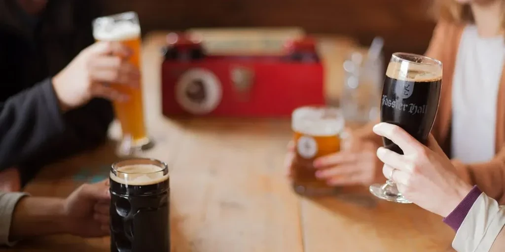Four hands hold various beer glasses, one etched 'Fassier Hall'.