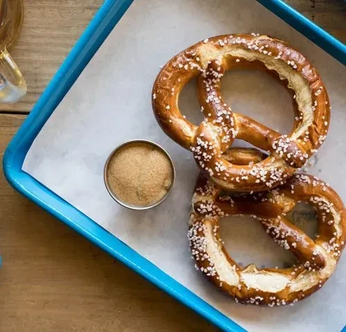 Two salted soft pretzels with dipping sauce in a blue tray.