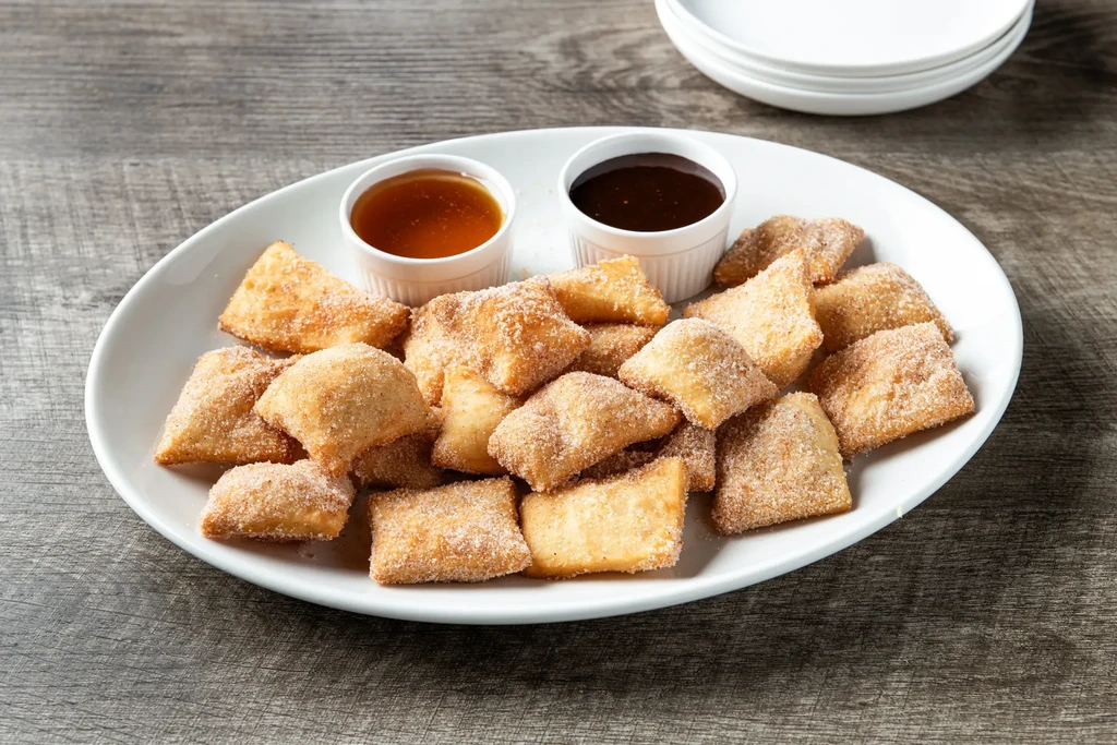 Oval plate with sugar-coated fried dough bites and two dipping sauces.