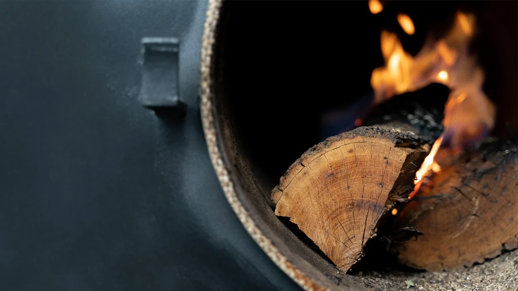 Burning split logs glow brightly inside a dark wood-fired chamber.