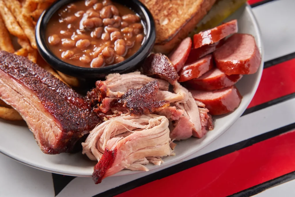 Hearty barbecue platter with various meats, baked beans, fries, and toast.