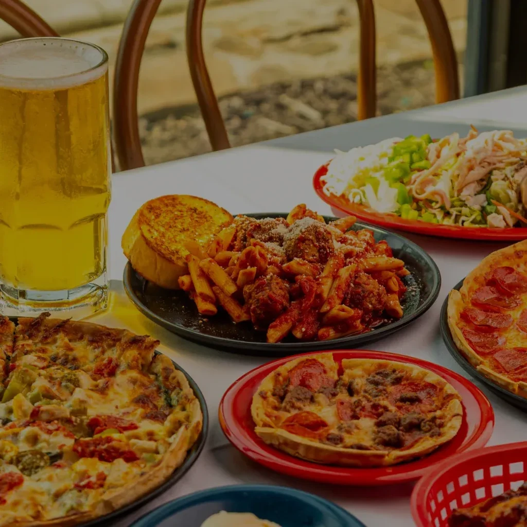 Two pizzas, pasta, salad, and beer on an outdoor table.