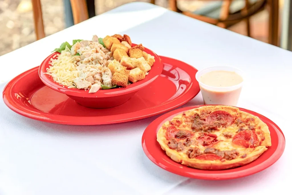 Chicken Caesar salad and pepperoni pizza served on red plates.