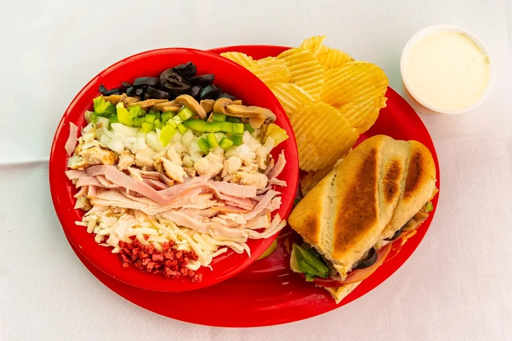 Sub sandwich, salad bowl, ruffled chips, sauce on a red platter.