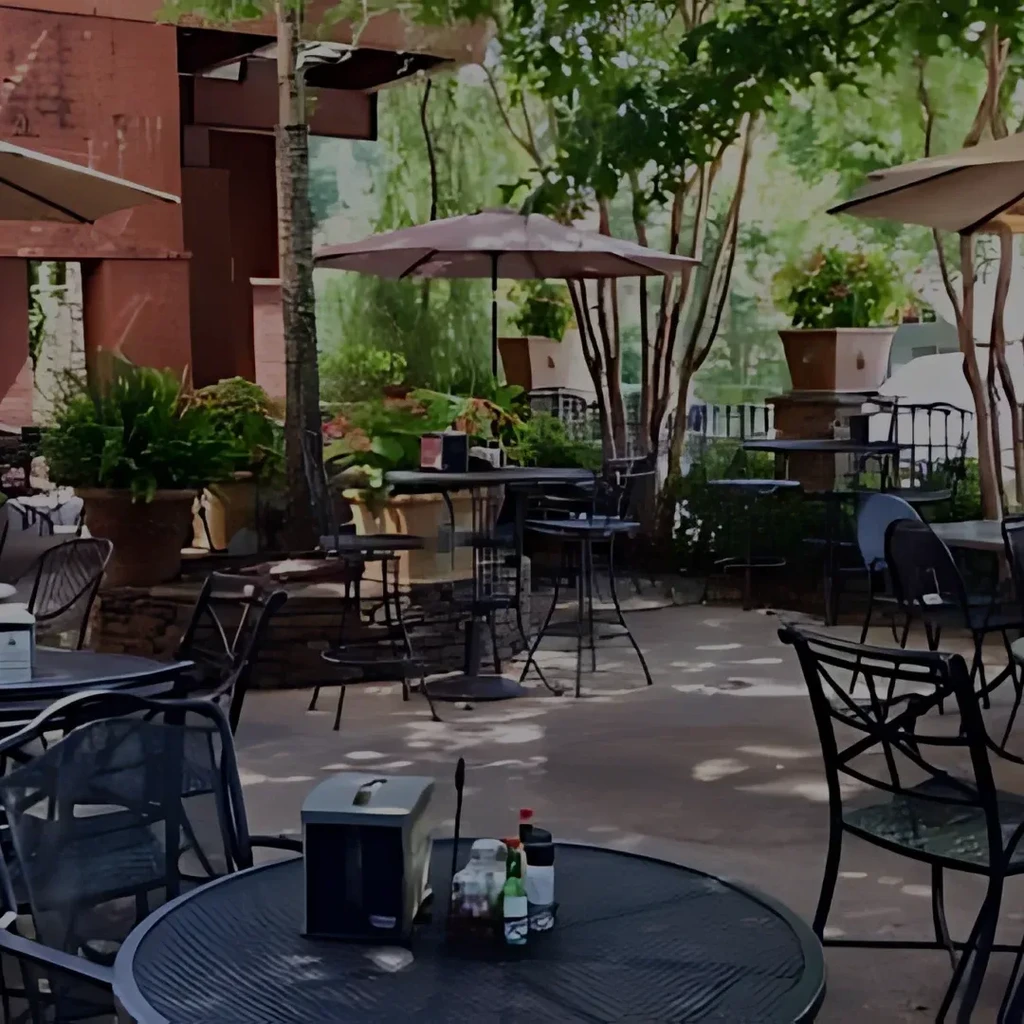 Outdoor restaurant patio with tables, umbrellas, and lush greenery.