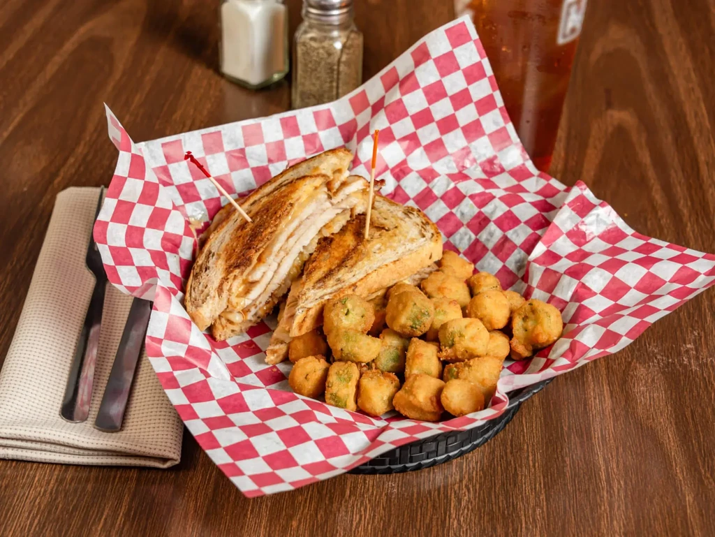 Grilled sandwich and fried sides in a basket on a wooden table.