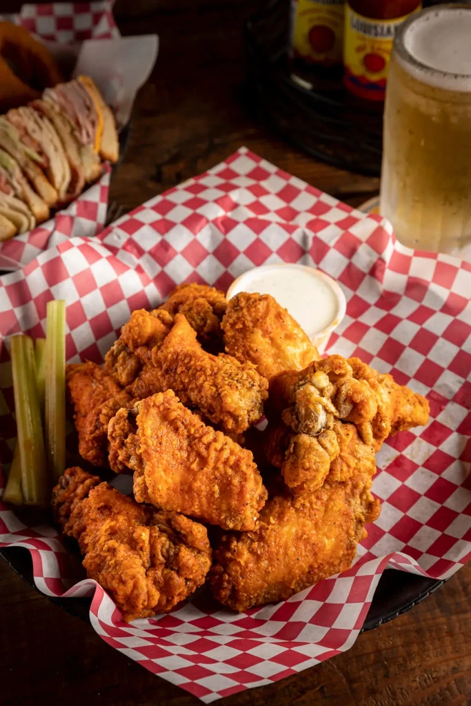 Golden-brown fried chicken wings, dipping sauce, celery, and cold beer.
