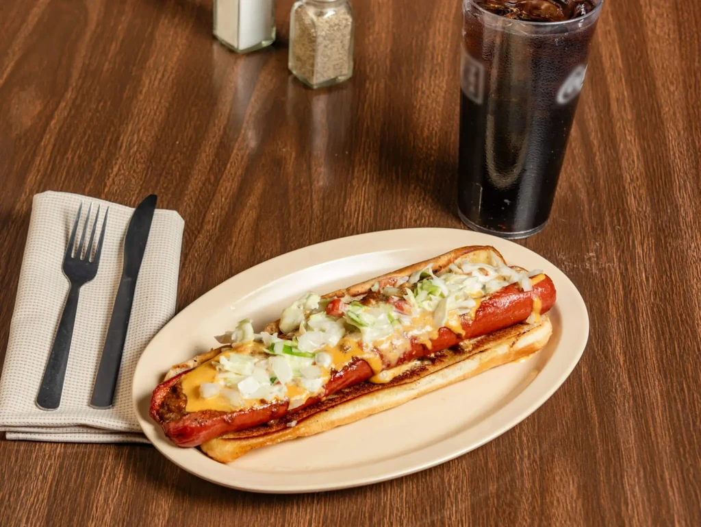 Chili cheese hot dog with onions and cabbage on a wooden table.