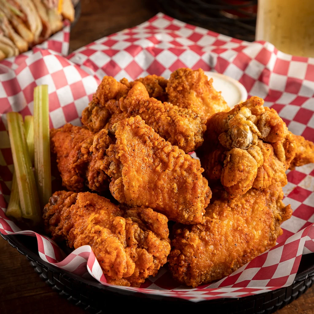 Basket of crispy fried chicken wings, celery, and dipping sauce.