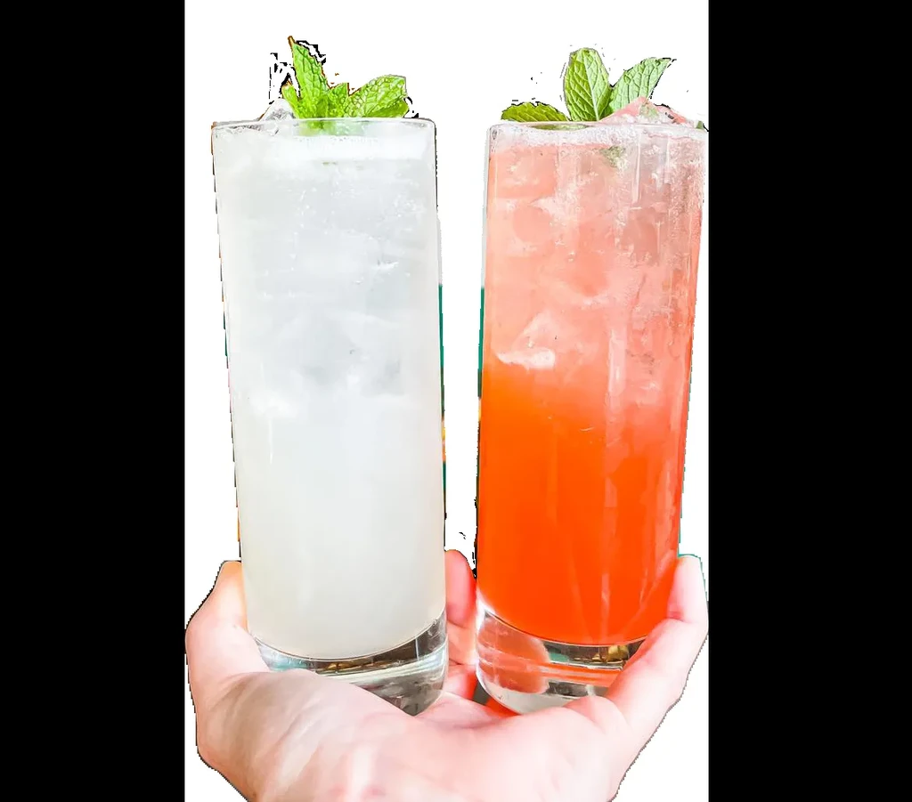 Two hands hold tall glasses with white and orange drinks, ice, mint.