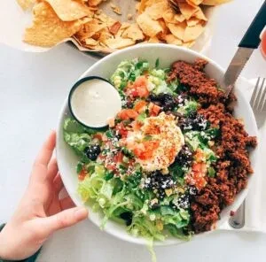 Overhead photo of a large taco salad with meat, vegetables, and dressing.