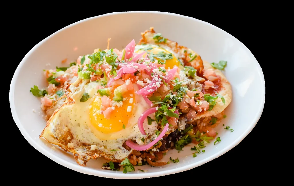 Close-up of fried eggs with tomatoes, cilantro, cheese, and pickled onions.