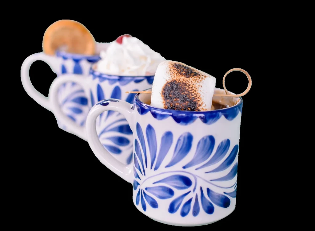 Three white Talavera mugs with marshmallow, whipped cream, and orange on black.