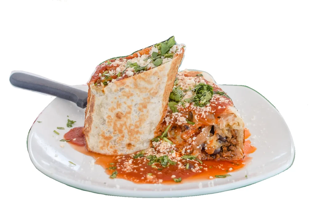 Halved burrito on plate, revealing meat filling, red sauce, cheese, herbs.