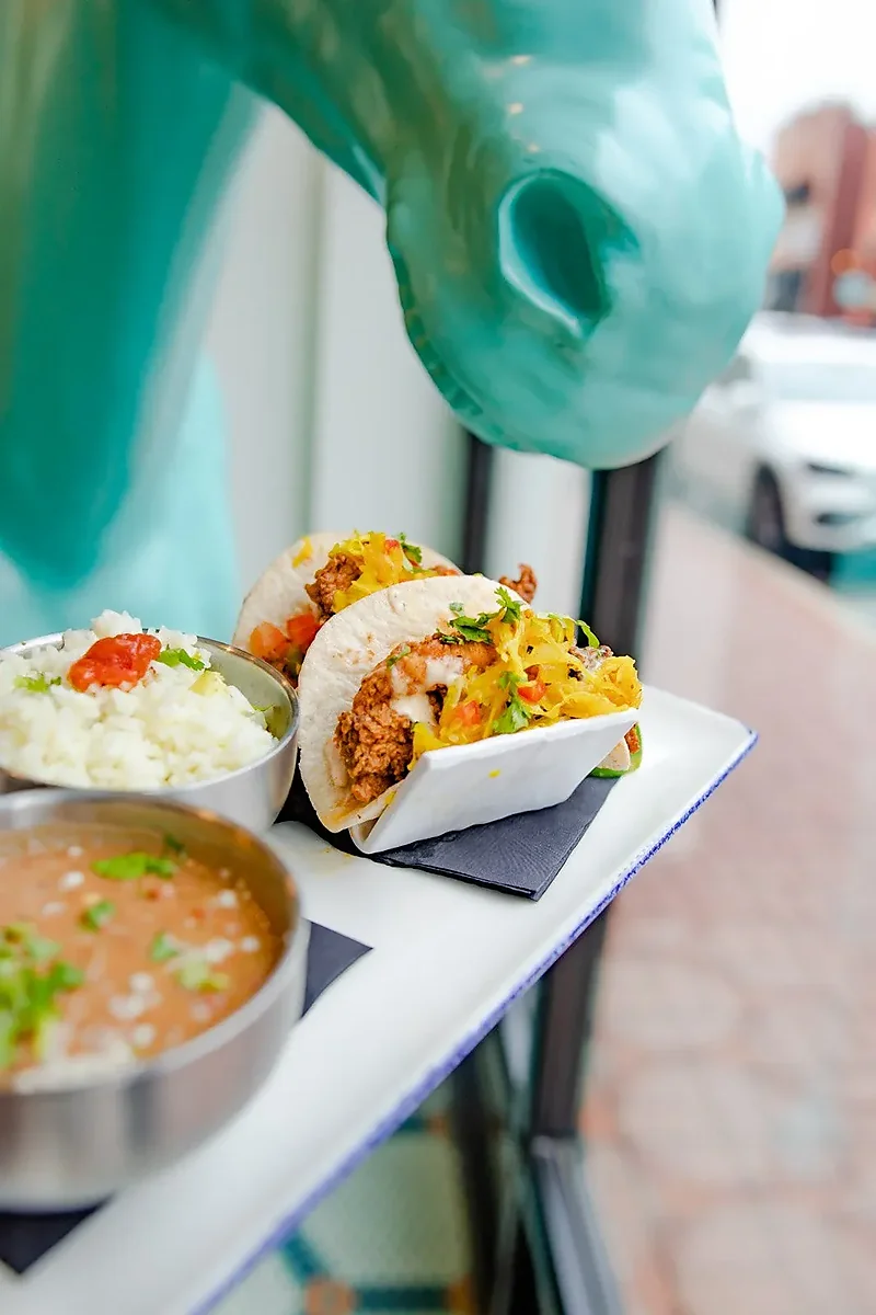 Two fried chicken tacos with rice and beans on window ledge