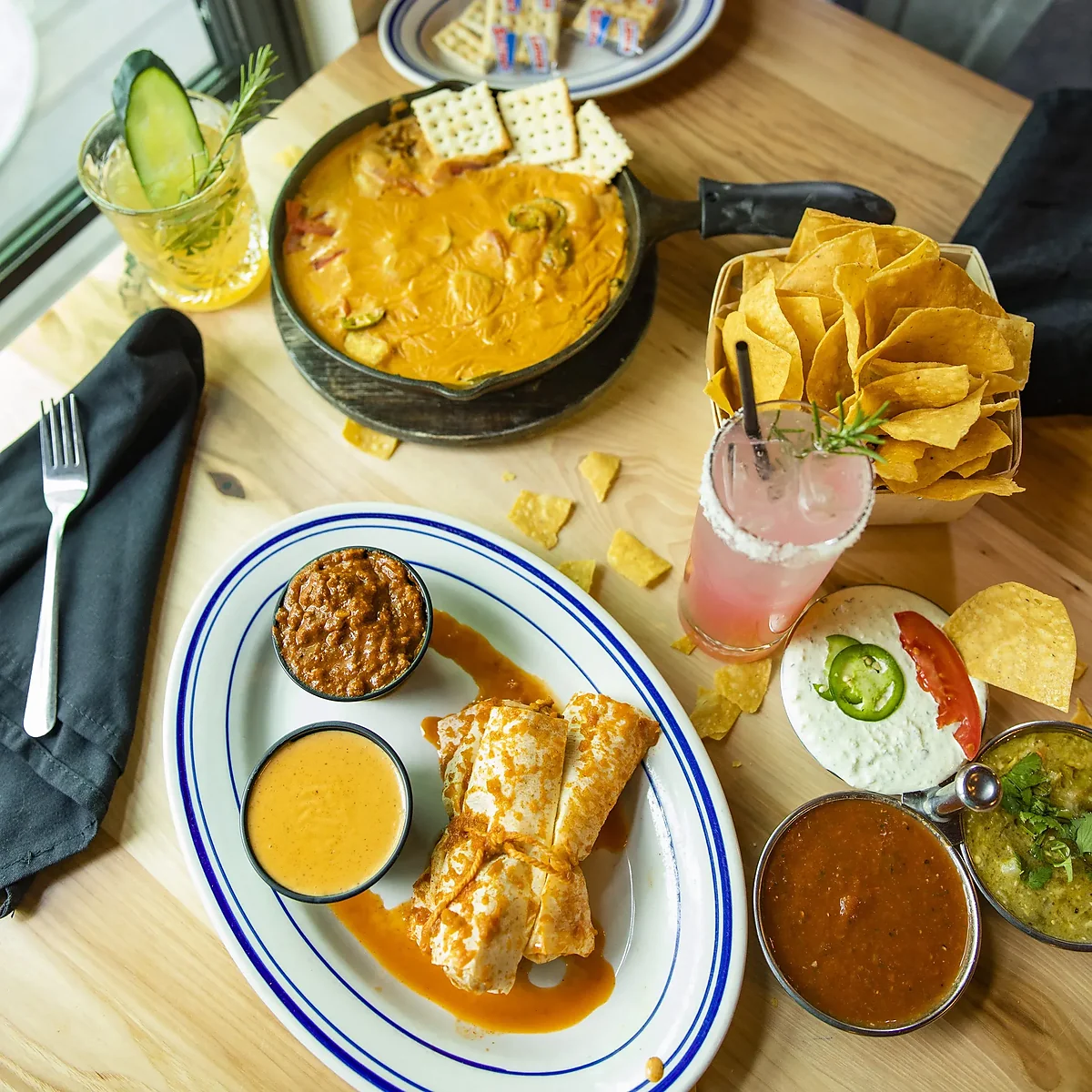 Table spread of cheese dip, enchiladas, chips, salsas and cocktails