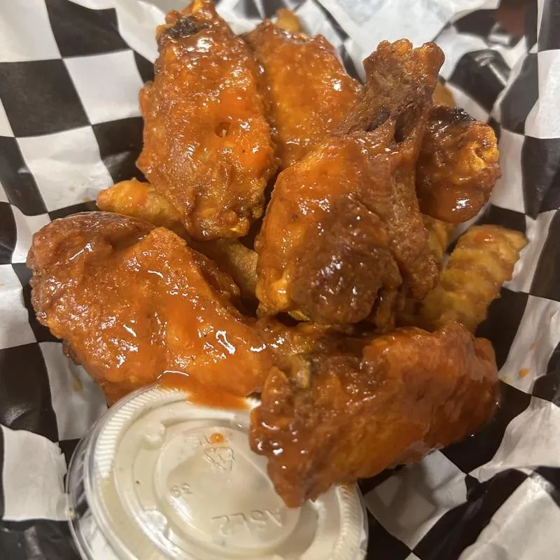 Glossy orange-red wings, fries, and dipping sauce in a checkered basket.