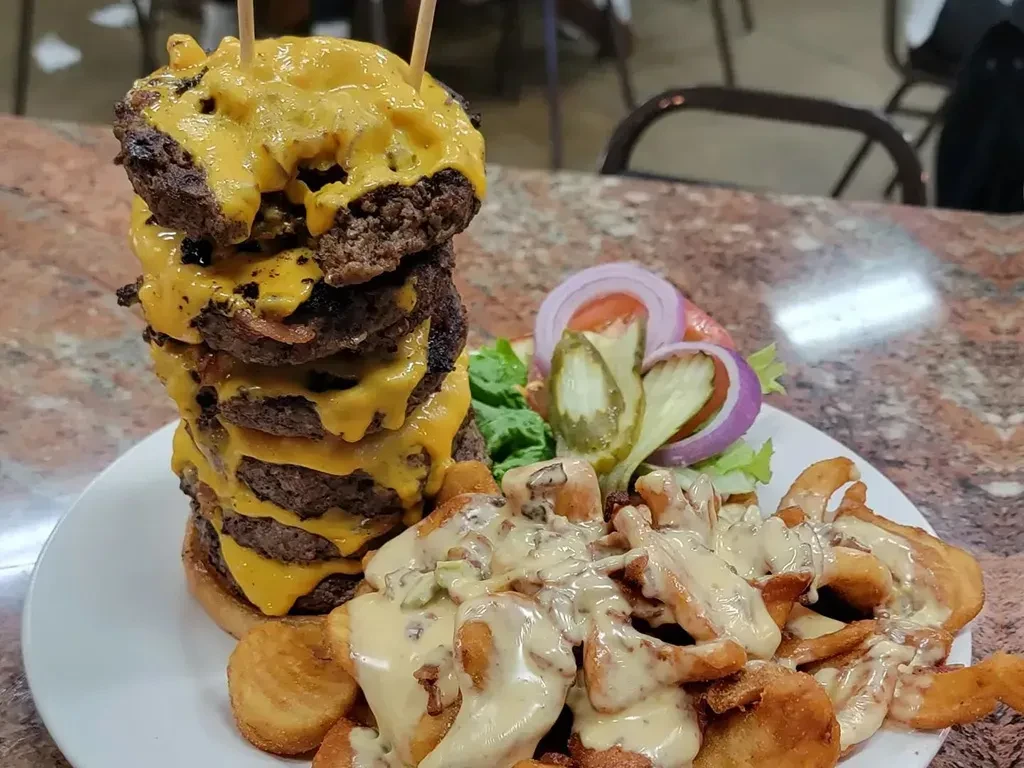 Towering five-patty cheeseburger, loaded fries with creamy sauce, and small salad.